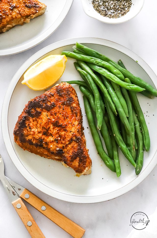 Blackened Tuna on a plate with green beans and a lemon wedge