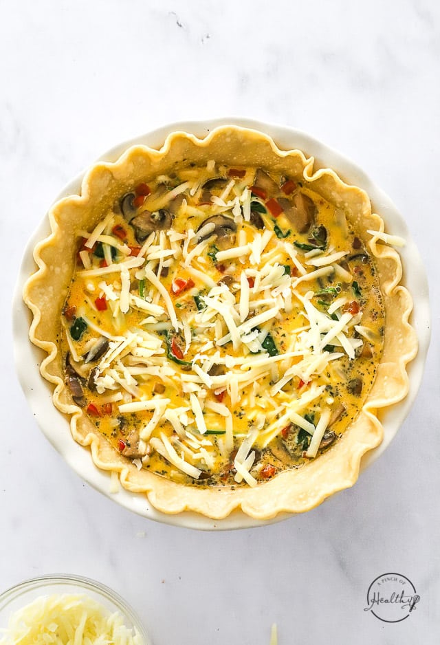 Assembled unbaked vegetarian quiche with cheese added on top