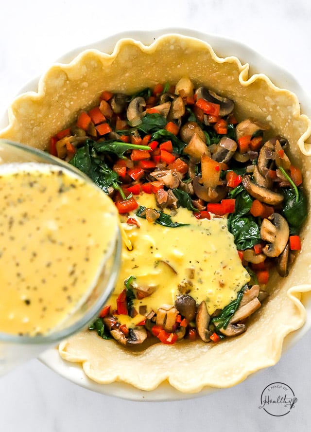 Pouring the egg mixture into the pie crust on top of the cooked veggies