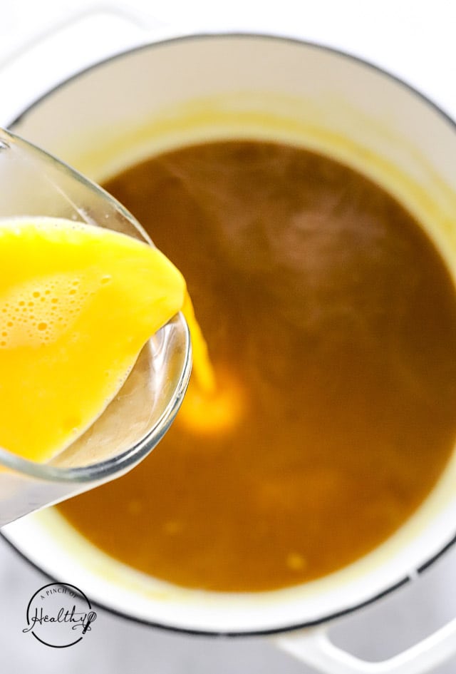 pouring eggs into broth to make egg drop soup