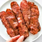 Woman's hand reaching for air fryer turkey bacon on white plate