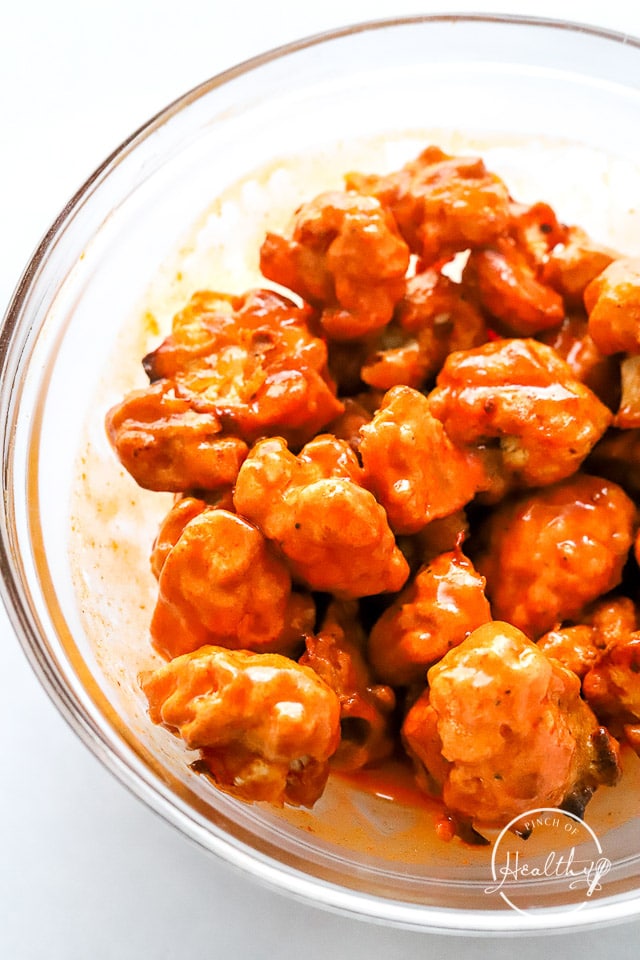 Cauliflower tossed in buffalo sauce in a glass bowl