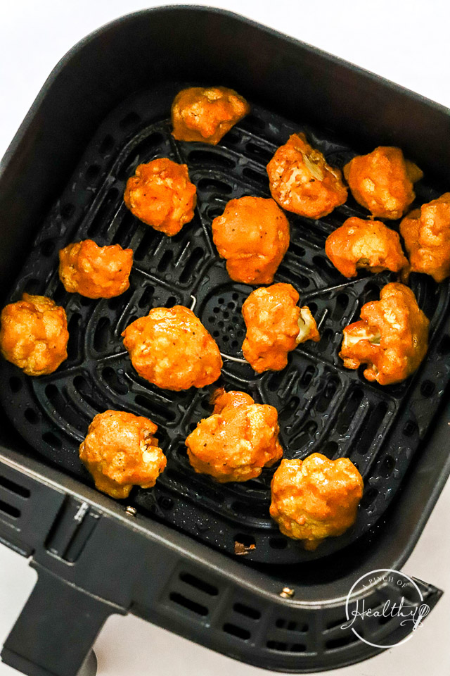 Coated cooked cauliflower in air fryer basket
