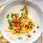 Instant Pot Potato Soup in a bowl with cheese, bacon and chives with spoon in a bowl