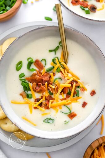 Instant Pot Potato Soup in a bowl with cheese, bacon and chives with spoon in a bowl