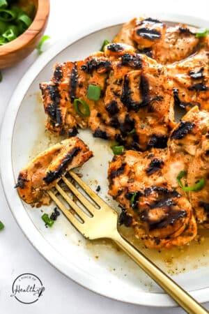 grilled chicken thighs sprinkled with parsley on a white plate with fork