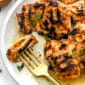 grilled chicken thighs sprinkled with parsley on a white plate with fork