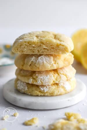 Lemon Crinkle Cookies stacked vertically on a white marble dish