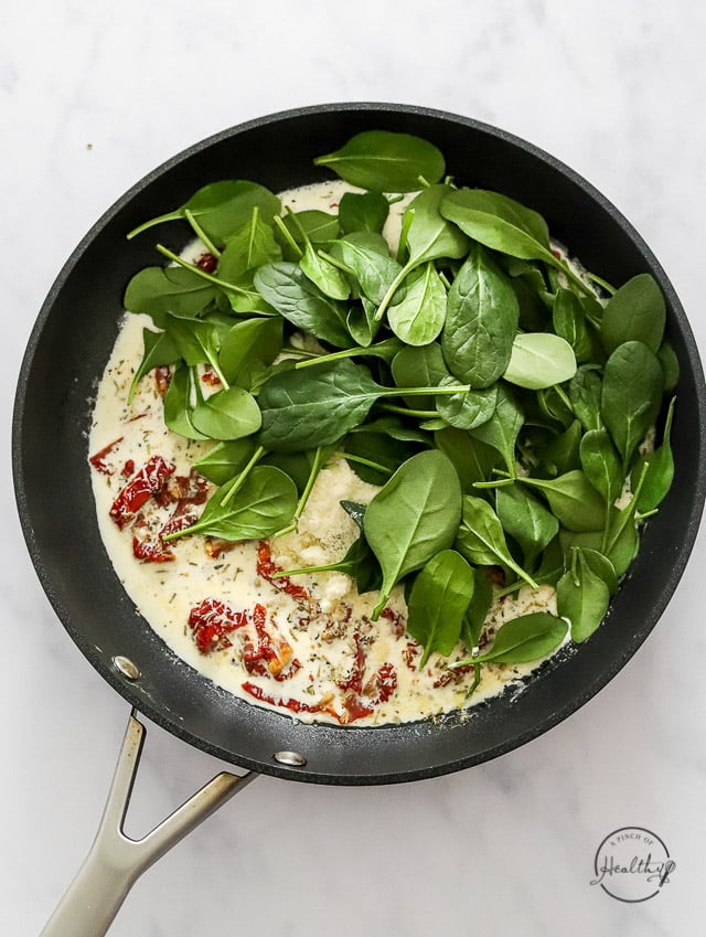 adding spinach to creamy sauce in a pan