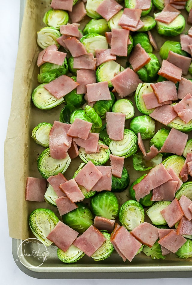 Brussel sprouts on baking sheet with chopped uncooked bacon