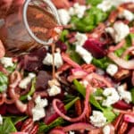 Hand pouring dressing over beet salad with goat cheese