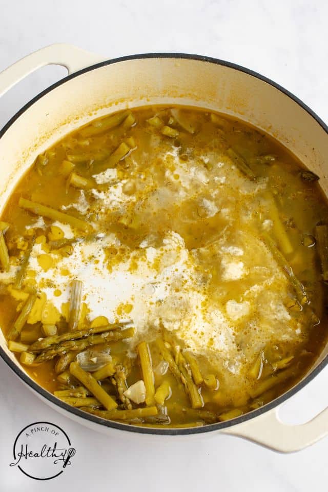 Cream being added to the cooked soup in a Dutch oven
