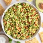 avocado salsa pictured on a white background with tortilla chips scattered around.