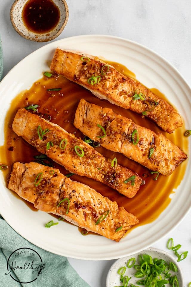 Four pieces of finished honey-glazed salmon on a white plate.
