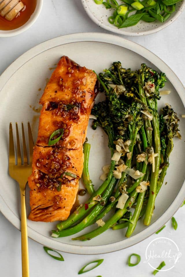 Finished honey glazed salmon shot from overhead on a white plate with broccolini and a gold fork