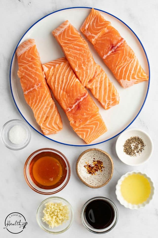 ingredients for honey glazed salmon on a white plate with a blue rim and the ingredients in separate bowls