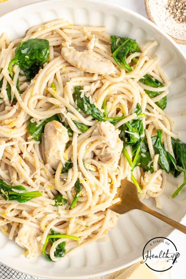 pasta with spinach and chicken in a lemon sauce in a large white scalloped bowl.