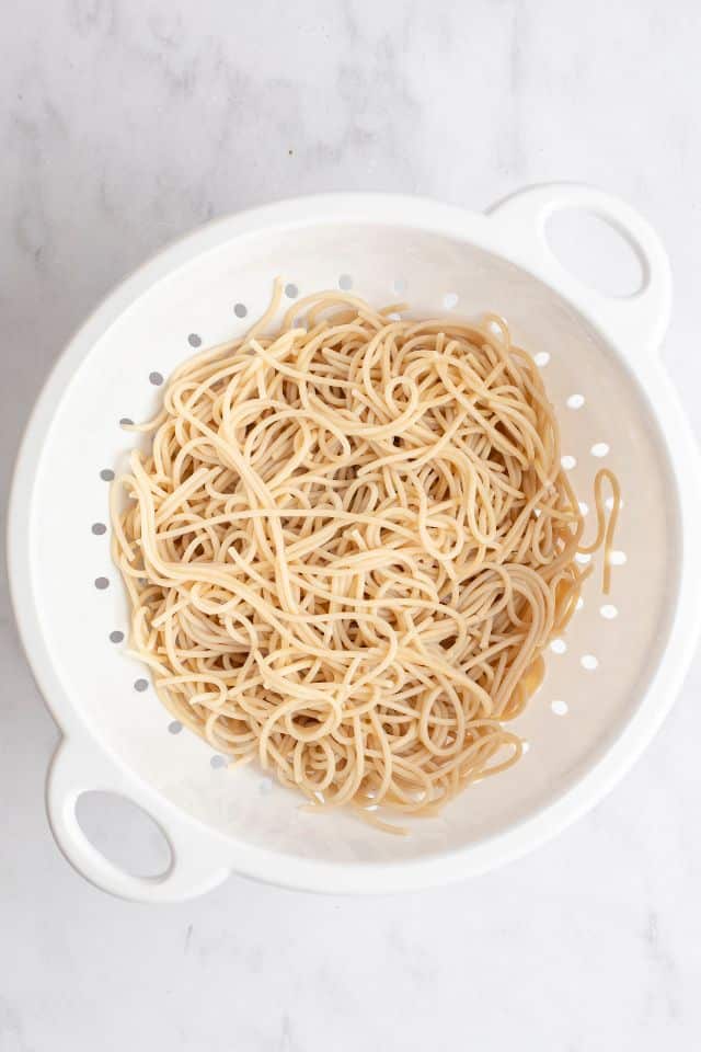 cooked spaghetti in a white colander on a marble background.