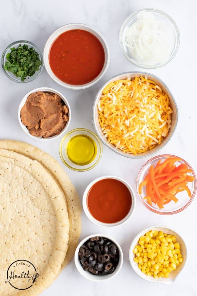 Mexican pizza ingredients on a white background in separate bowls.