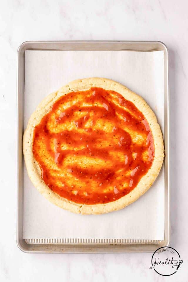 pizza crust with taco sauce spread evenly over it on a parchment-lined baking sheet.