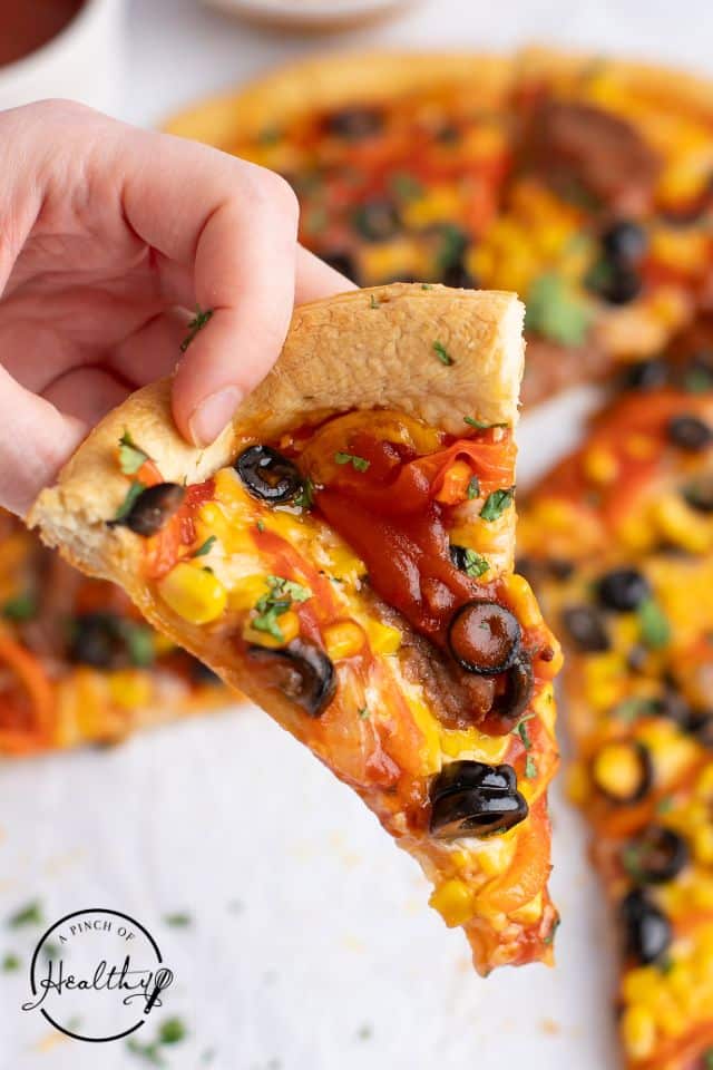 A slice of Mexican Pizza being held up to the camera.