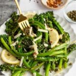 sauteed broccolini on a white plate with a gold fork grabbing a bite