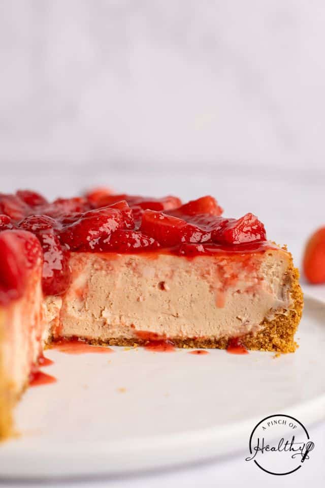 strawberry cheesecake with several pieces cut out of it, shot from the side