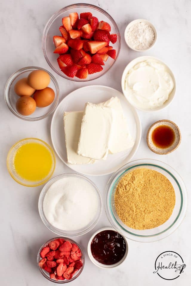 Ingredients for Strawberry Cheesecake on a white background in separate containers shot from overhead.