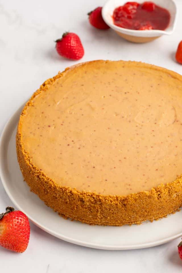 Baked cheesecake on a white plate before being topped with strawberry mixture