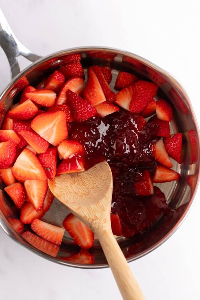 Ingredients for strawberry sauce in a pan with a wooden spoon