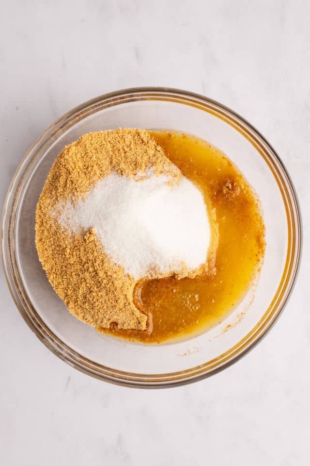 Graham cracker crumbs with sugar and butter in a mixing bowl, before being combined.
