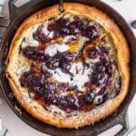 Blueberry Dutch Baby in a cast iron pan with maple syrup and blueberry syrup on top