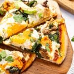 Breakfast pizza cut into slices on a wooden cutting board.