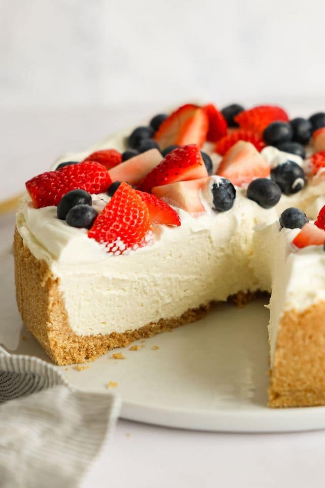 No bake cheesecake with a slice taken out of it and fresh berries on top.