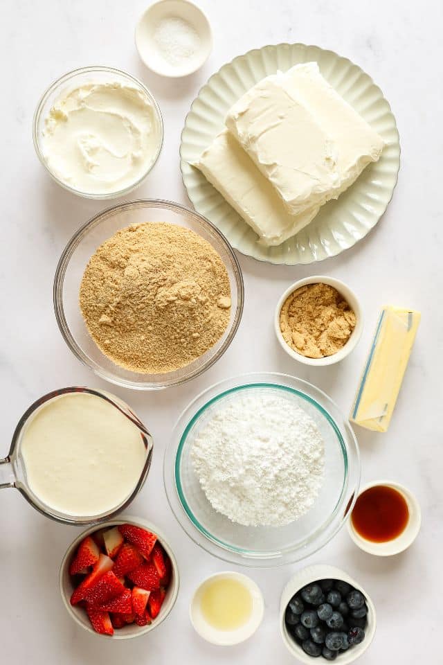 Ingredients for no-bake cheesecake in separate containers on a white background.