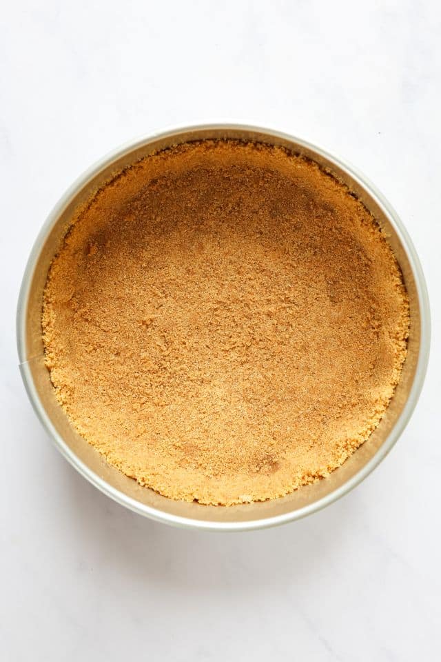 Graham cracker crust pressed into a springform pan on a white background.