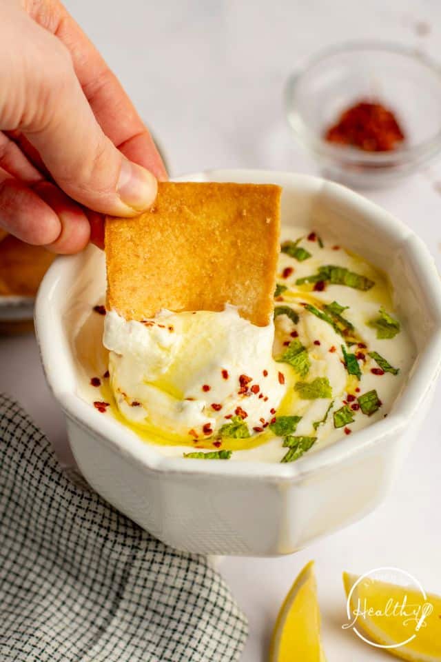 Whipped Feta Dip with a pita chip being dipped into it, in a white serving dish.