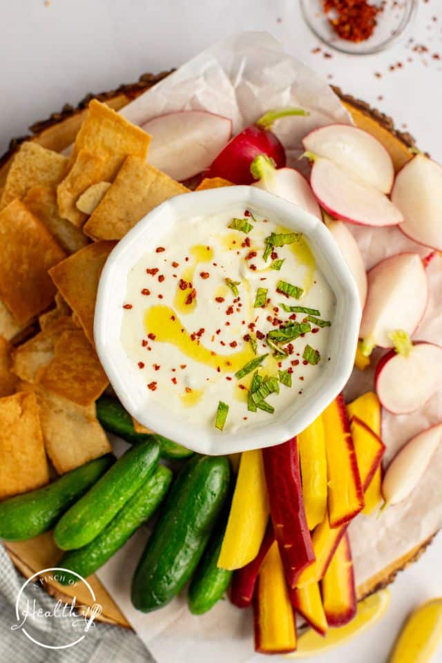 Finished whipped feta dip on a serving tray with vegetables, pita chips, and garnish on top.