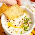 Whipped feta dip in a white dish being scooped out by a pita chip.