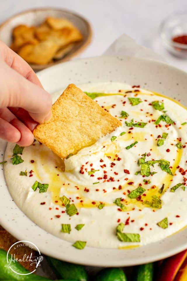Finished whipped feta dip in a serving container with mint, olive oil, and red pepper flakes on top.