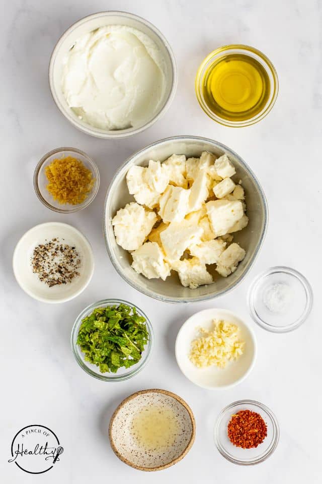 Ingredients for whipped feta dip on a white background in separate containers. 