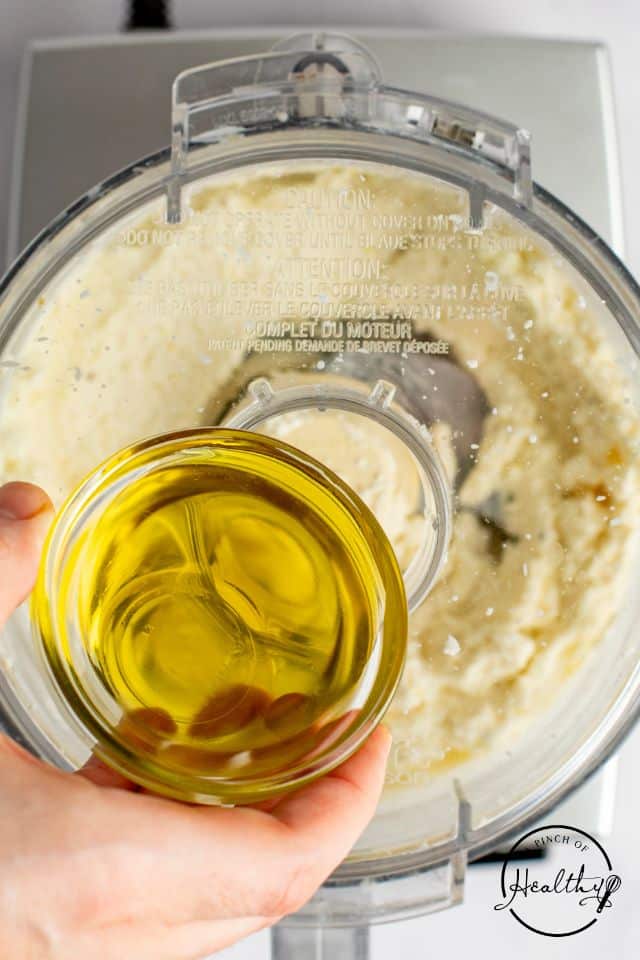 Olive oil being added slowly to the blended feta mixture.