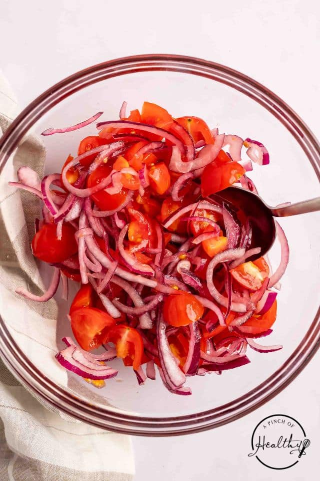 Tomato onion salad in a glass bowl after being mixed.