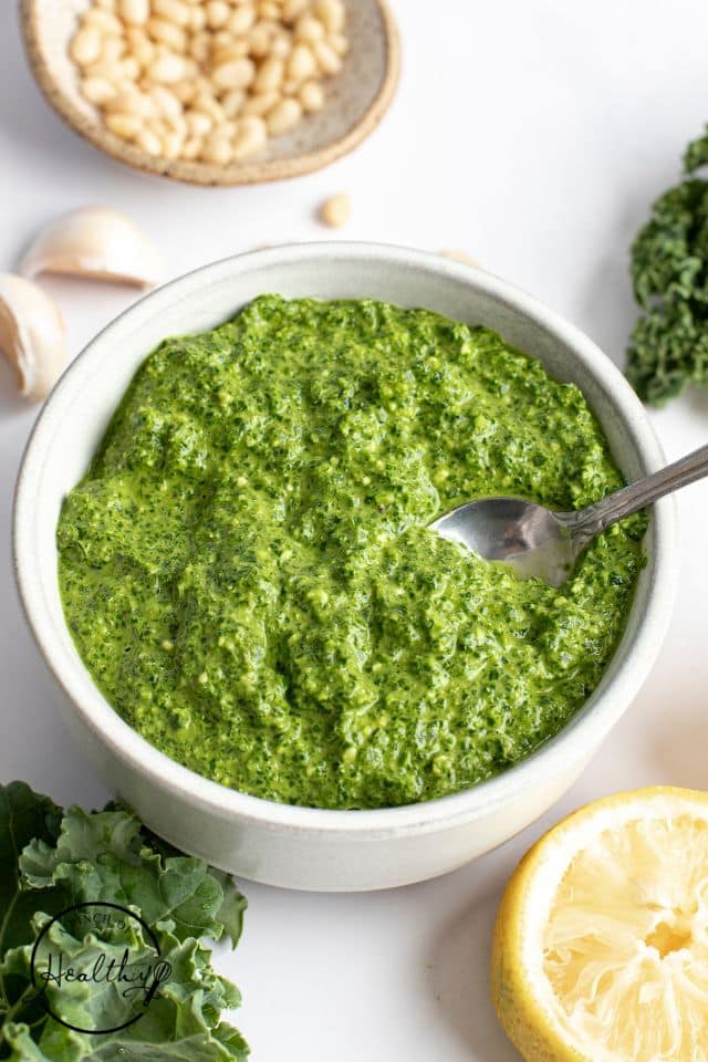 Finished kale pesto in a white bowl with a silver spoon in the bowl.