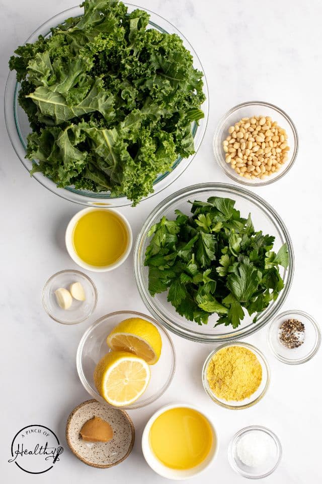 Ingredients for kale pesto in individual bowls on a white background.