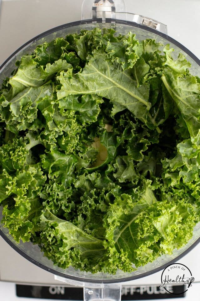 Fresh kale added to a food processor before being processed.