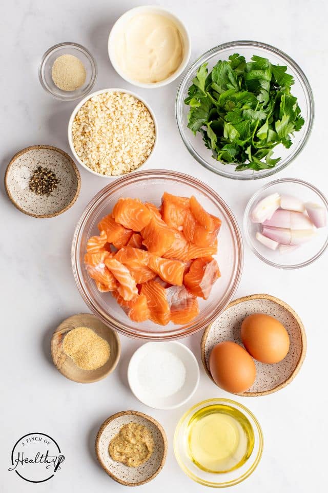 Ingredients for fresh salmon cakes on a white background in separate dishes.