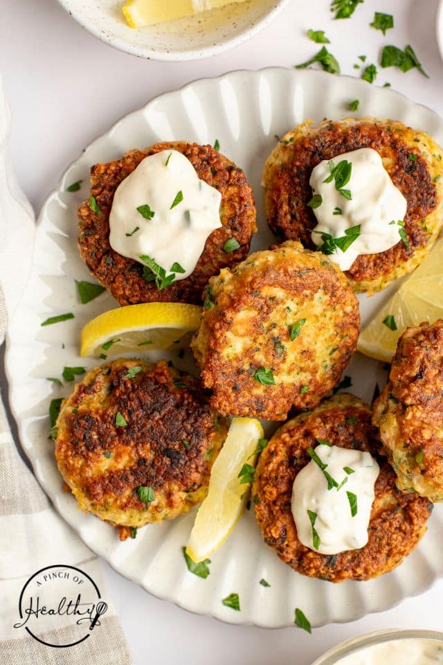A plate of salmon cakes on a white platter with fresh lemon slices.