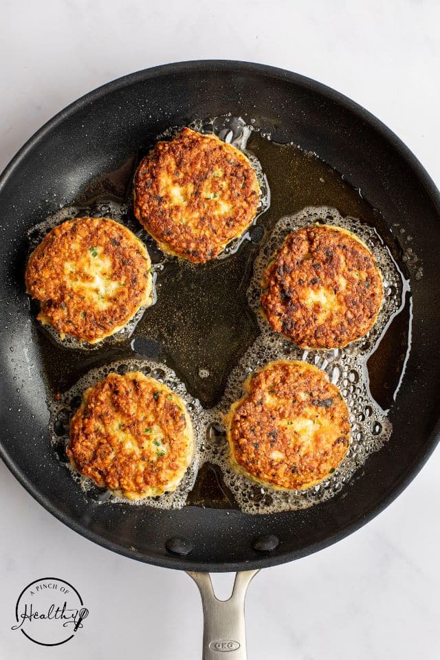 Salmon cakes in a pan being shallow-fried in oil.