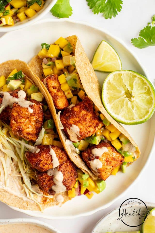 Salmon tacos with lime and cilantro on a white plate.